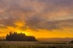 A stupendous sunset lights up the dramatic clouds above the Cluxewe River Estuary on Northern Vancouver Island, Canada, and the long reed grass and channel of the Cluxewe River glint in the light of sunset.