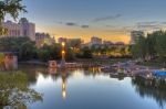 The still waters of the Assiniboine River reflect the lights of the marina and surrounding buildings at The Forks National Historic Site during dusk in the city of Winnipeg, Manitoba, Canada.