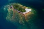 A tiny forest clad island sits like an oasis in the cool blue waters of Lake Superior in Ontario, Canada. The island appears to emerge from the depths of the lake on angled slabs of rock.