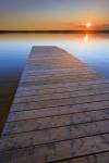 Stretching out like an oasis in the middle of Manitoba, Lake Audy in Riding Mountain National Park is a popular destination for both visitors and residents of Canada. In this picture of a wooden wharf leading off towards the sunset, the lake has been turn