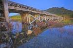 An old bridge is reflected on the surface of pristine Kennedy Lake on a clear Vancouver Island day.