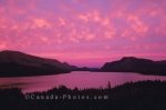 A vivid pink sunset reflects in the clouds above Trout River Pond in Gros Morne National Park, Newfoundland, Canada.