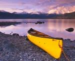 Barely a ripple can be seen on the water of Kluane Lake behind this yellow canoe as the sunset reflects perfectly on its surface. Kluane Lake is situated in the wilderness of Kluane National Park in the Yukon, Canada.