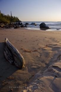 Soft sand lines the beach at Katherine Cove in Lake Superior Provincial Park in Ontario, Canada surrounded by a rocky shoreline on either side.