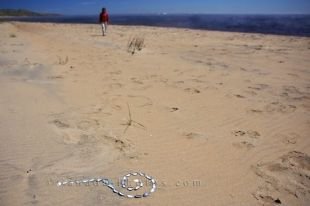 A woman strolls on the sandy beach along the Pinware River in Southern Labrador, nearing a display of shell art.