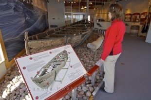 A tourist to the Red Bay National Historic Site of Canada in Labrador strolls through the Interpretation Centre and stops at an exhibit of an ancient whaling boat and wall mural.